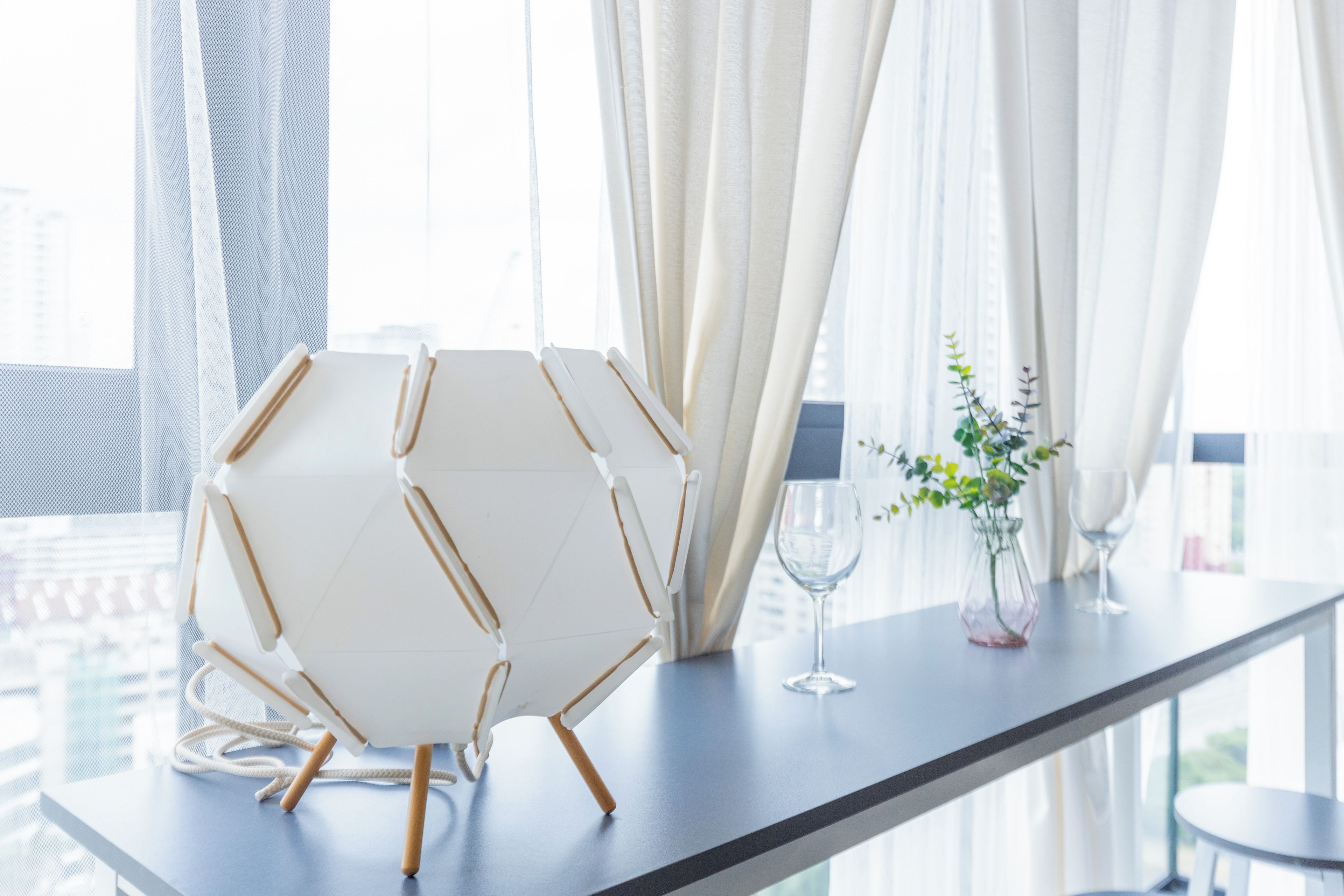 A modern interior with a white hexagonal chair, a glass vase with a plant, and two wine glasses on a table.
