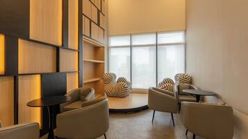 A modern lounge area with a circular seating arrangement, a large window with a city view, and built-in wooden shelving.