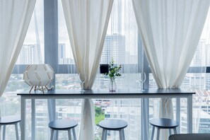 A modern room with a glass table, four stools, a decorative chair, and a vase with a plant. - Urban Suite Penang (George Town)