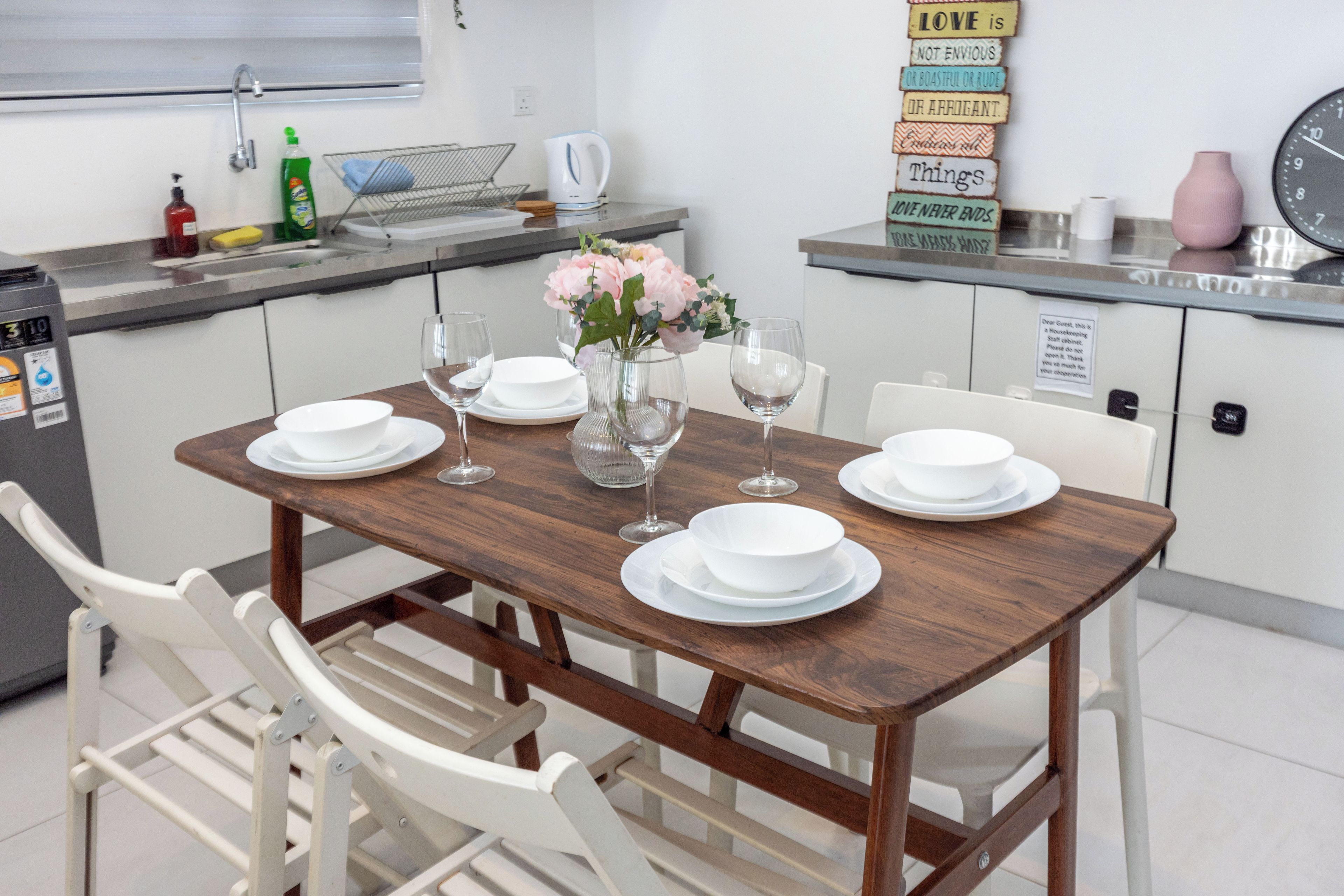 Un coin repas avec une table en bois dressée pour quatre personnes, des chaises blanches et un vase rempli de fleurs.