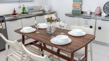 Un coin repas avec une table en bois dressée pour quatre personnes, des chaises blanches et un vase rempli de fleurs.