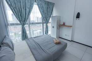 A bedroom with a bed, curtains, a wardrobe, and a view of the cityscape.