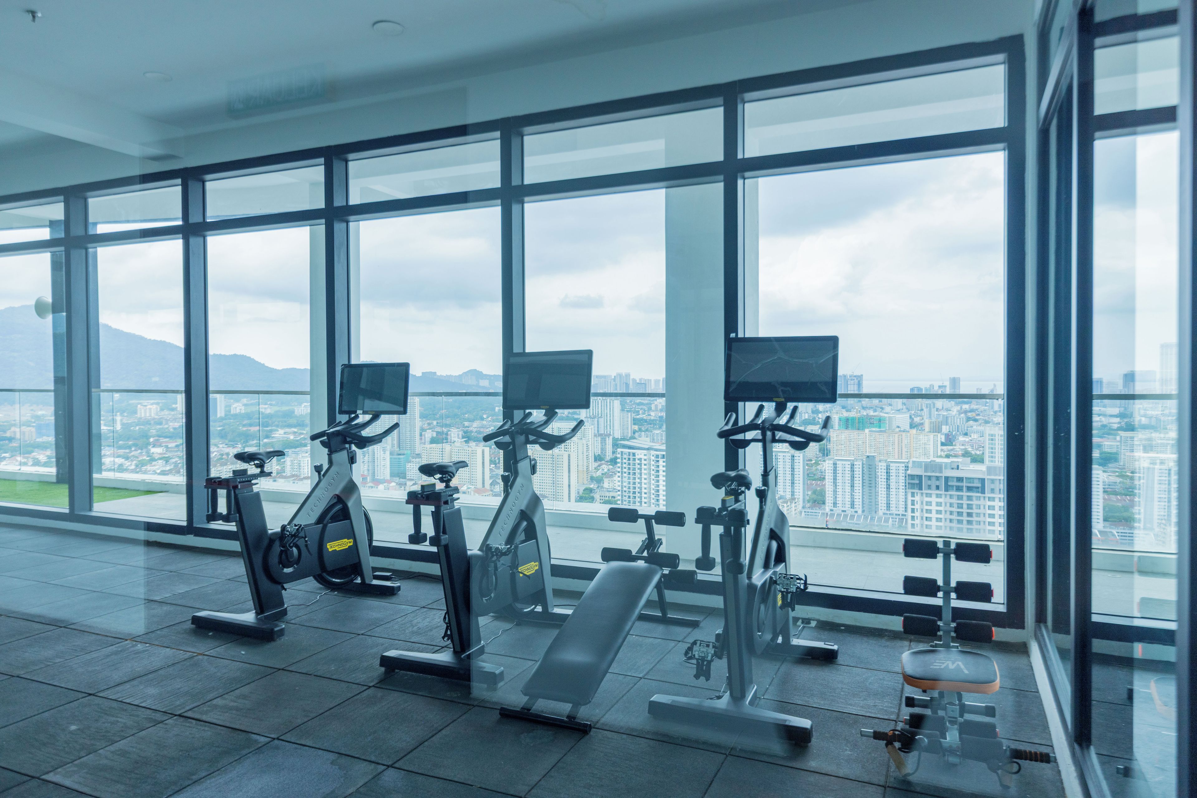 A gym with exercise equipment and large windows overlooking a cityscape.