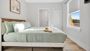 Ein Schlafzimmer mit Bett, Fenster mit Blick, Tür und einem gerahmten Bild an der Wand.
