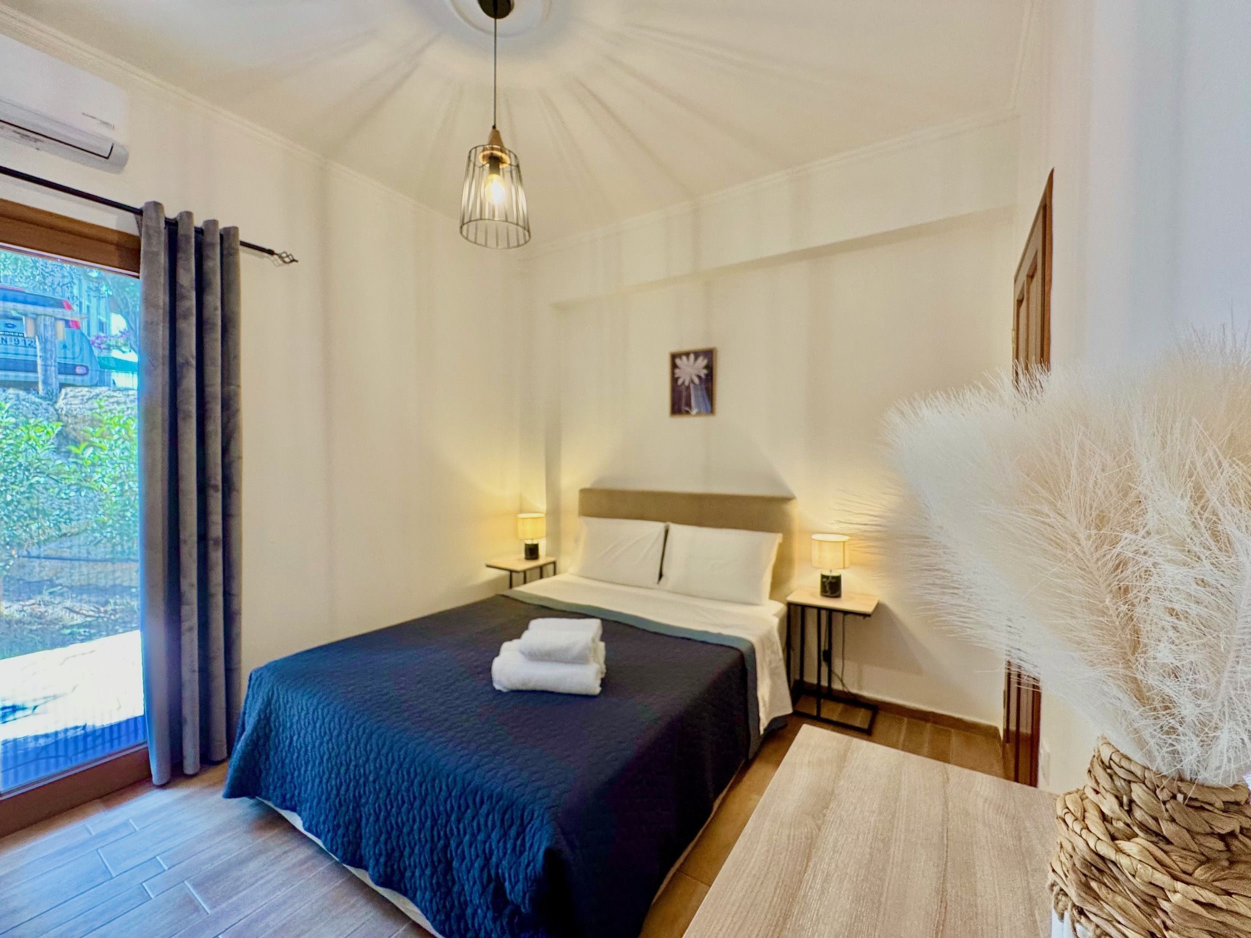 Habitación de hotel con cama, lámparas de noche, ventana con cortinas, luz de techo y un jarrón decorativo.