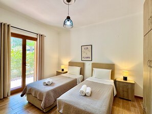 A hotel room with two beds, a sliding glass door, a ceiling light, and a wall-mounted picture.