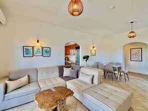 Ein modernes Wohnzimmer mit einer Eckcouch, einem Couchtisch und einem Essbereich mit Stühlen.
