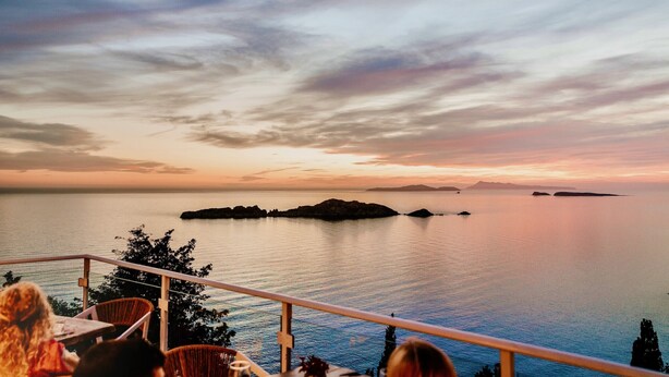A terrace with a view of the sea and islands at sunset.