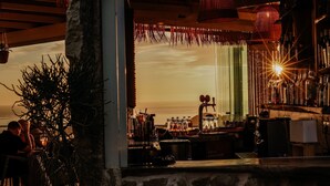 A bar area with a rustic stone wall, a wooden ceiling, and a view of the sunset.