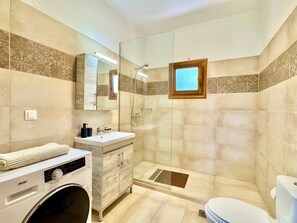A bathroom with a washing machine, a sink, a toilet, and a shower area.