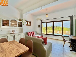 Una habitació àmplia amb un gran finestral, zona de menjador i un sofà amb coixins vermells.