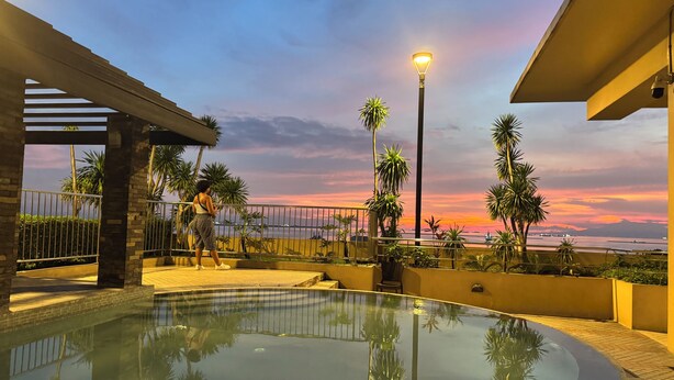 A pool area with a sunset view, palm trees, and a street lamp. - 康宿·海映居 | KanStay Oceanview Residence 4005 | 2BR 2BA · Manila Bay View (Manila)