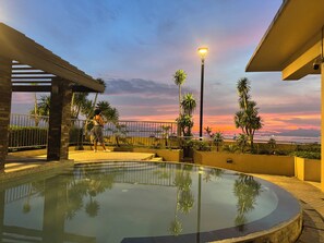 Ein Poolbereich mit Sonnenuntergangsblick, Palmen und einer Straßenlaterne.