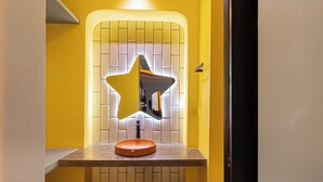 Un baño con un espejo en forma de estrella, un lavabo redondo y una pared con azulejos.