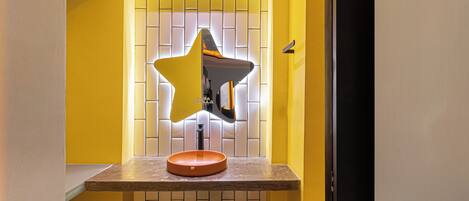 A bathroom with a star-shaped mirror, a round sink, and a tiled wall.