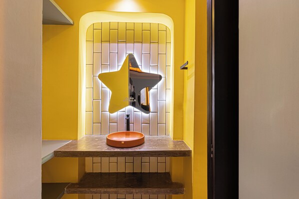 Un baño con un espejo en forma de estrella, un lavabo redondo y una pared con azulejos.