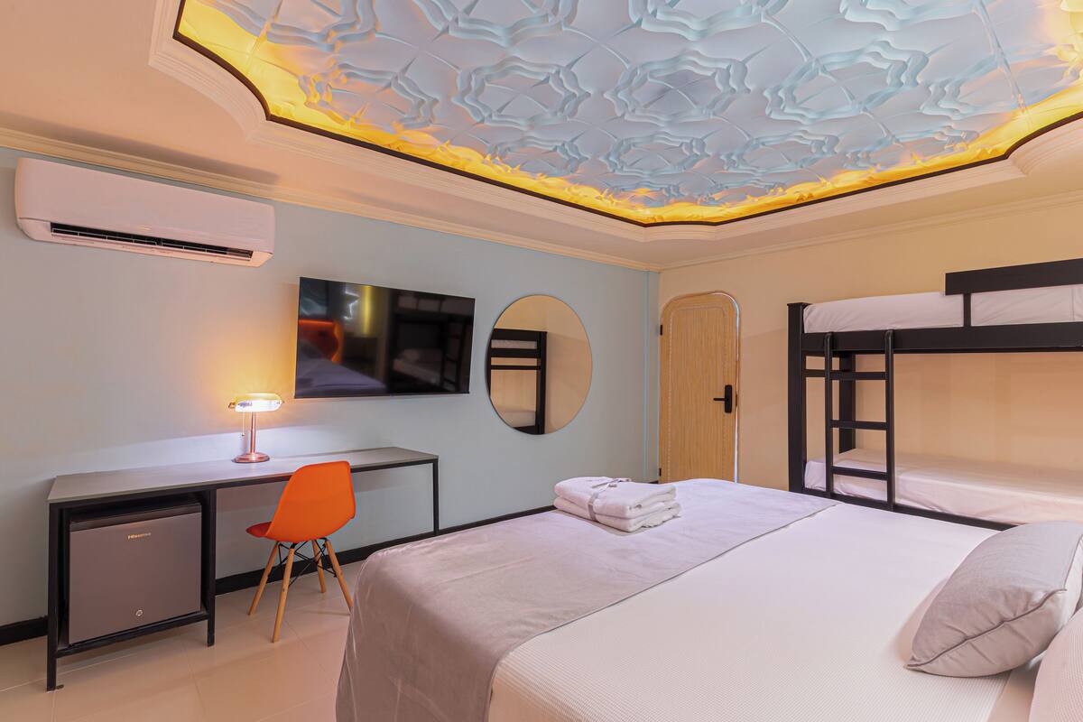 Une chambre d’hôtel avec un lit superposé, un bureau avec une chaise, une télévision et un plafond au design original.
