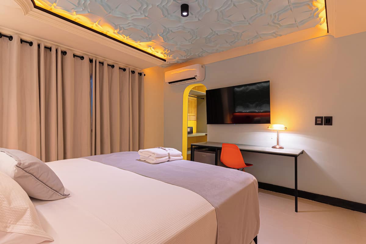 Une chambre d’hôtel équipée d’un lit, d’un bureau, d’un climatiseur, d’une chaise et d’un téléviseur fixé au mur.
