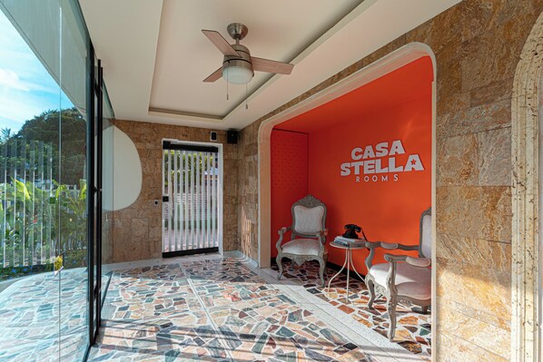 A hotel lobby with a tiled floor, a ceiling fan, and a sign reading "CASA STELLA ROOMS".