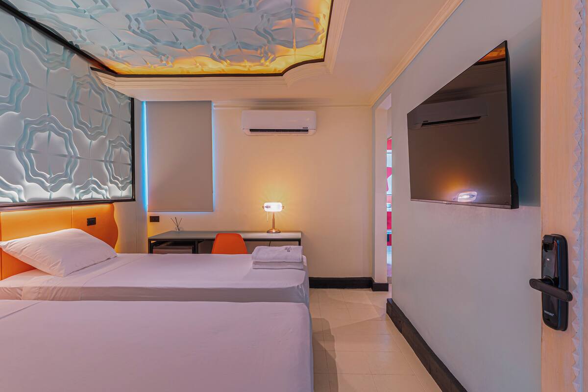 Une chambre d’hôtel avec deux lits, un bureau avec une chaise, un téléviseur fixé au mur et un appareil de climatisation.