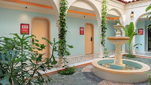 Vestíbulo de hotel con una fuente, suelo de baldosas y arcos.
