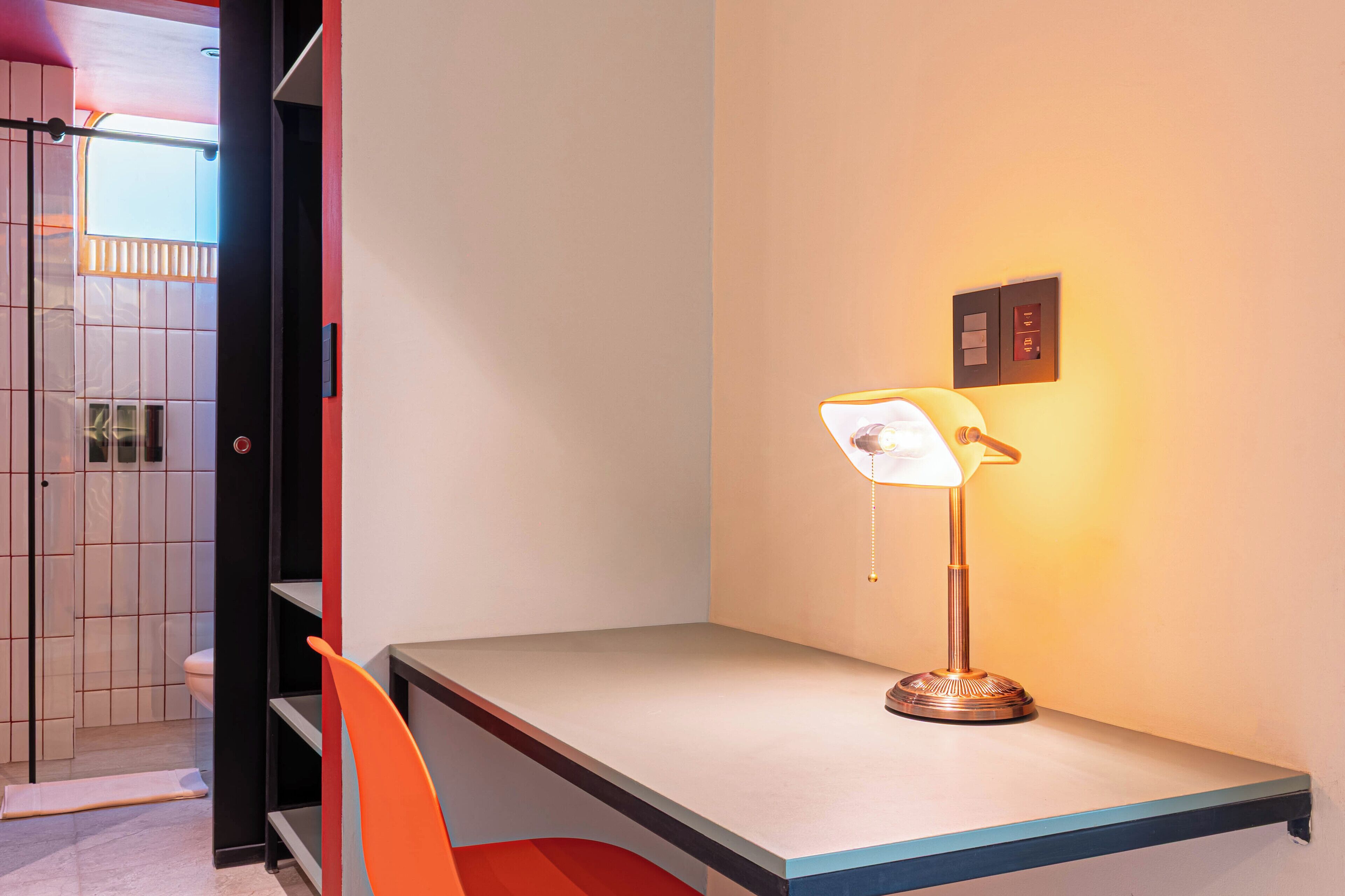 A hotel room with a desk, a chair, a lamp, and a view of the outside.