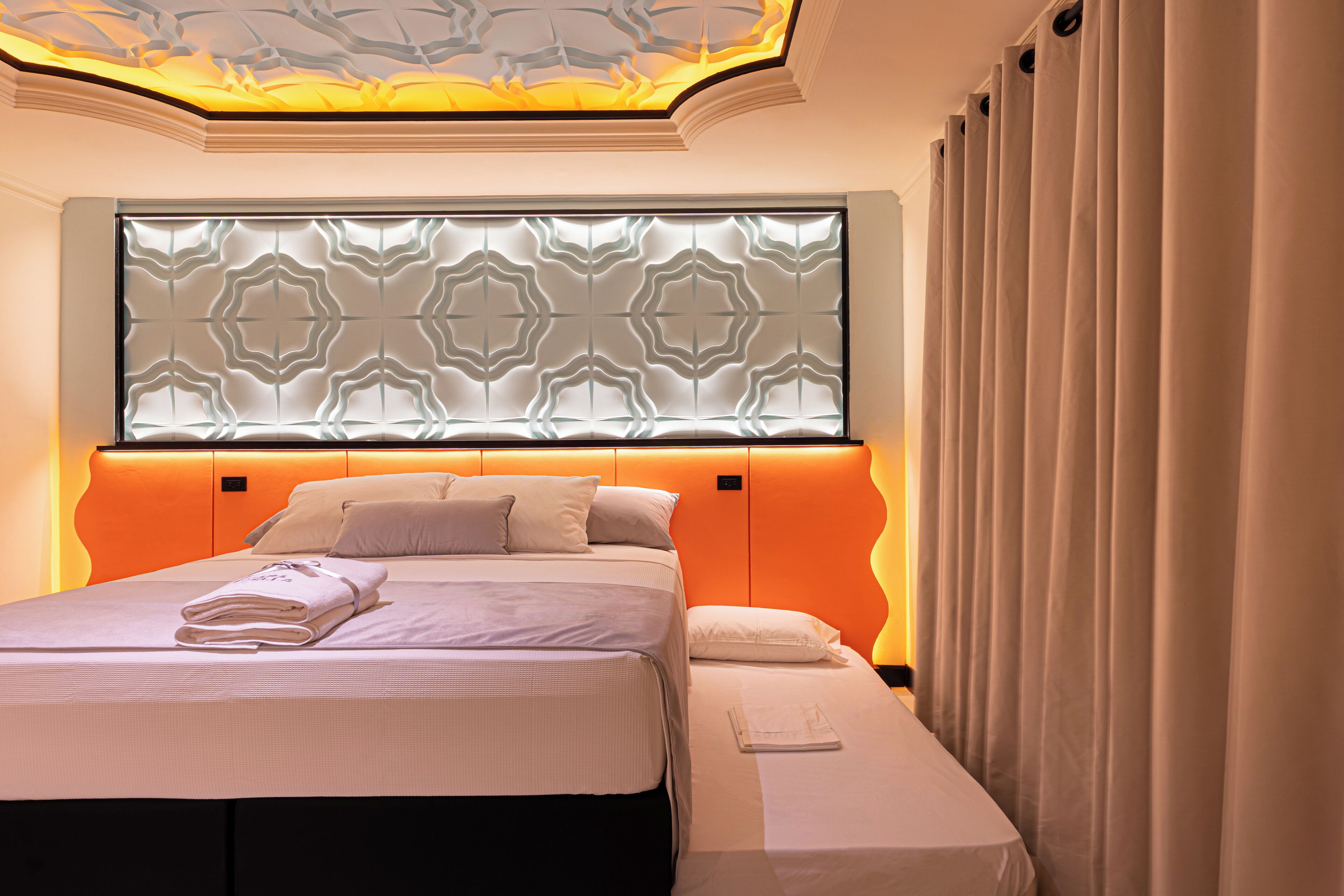 Una habitación de hotel moderna con una cama grande, un cabecero con diseño geométrico y una cortina a la derecha.