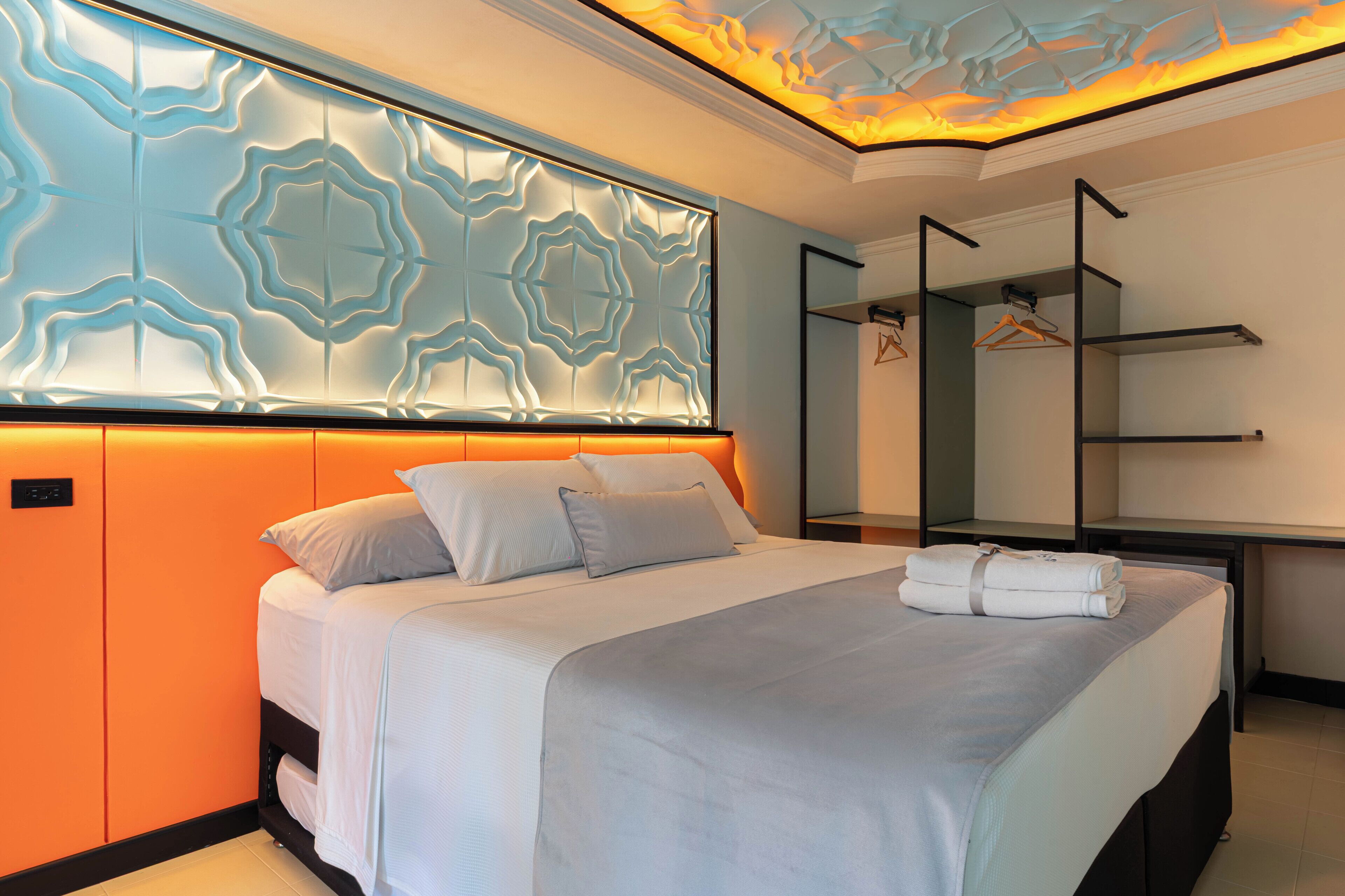 A modern hotel room with a large bed, a wall-mounted TV, a mirror, and a wardrobe.