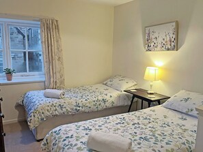 A bedroom with two beds, a window with curtains, a lamp, and a painting on the wall.