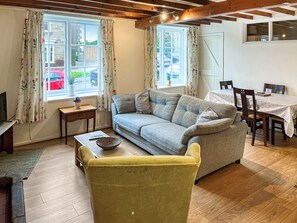 A cozy living room with a sofa, a yellow armchair, a wooden coffee table, and a dining table with chairs.