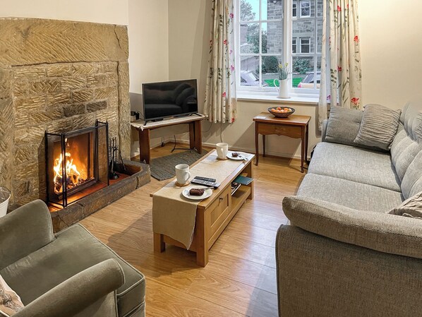 Una sala de estar acogedora con chimenea de piedra, un televisor sobre un soporte de madera, un sofá, una mesa de centro y una ventana con cortinas.