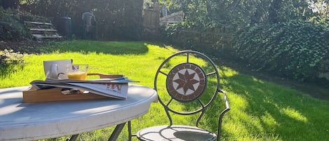 Una mesa redonda con una silla, un vaso de jugo de naranja y un libro.
