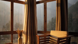 A wooden bench with a cushion, a vase with dried flowers, and a pine cone on a table by a window with curtains. - The Hidden Treasure (Sosan)