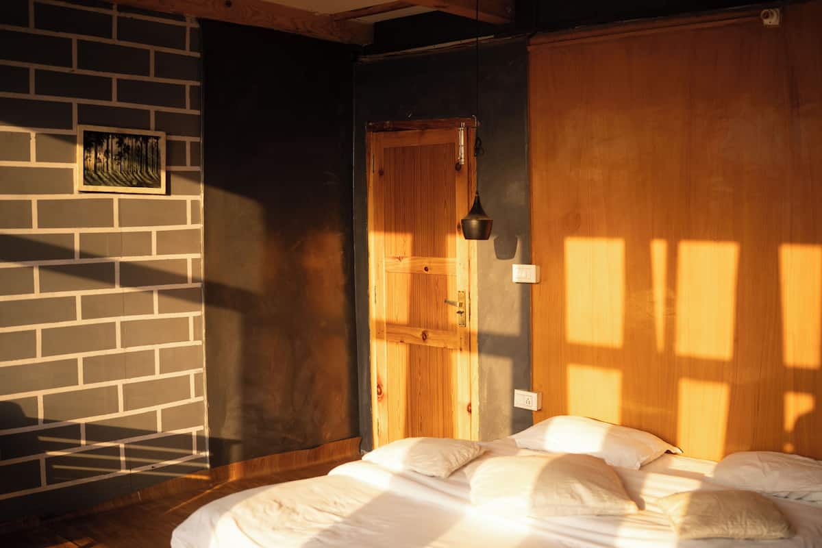 Una habitación con pared de ladrillo, puerta de madera, cama con ropa de cama blanca y una lámpara colgante.