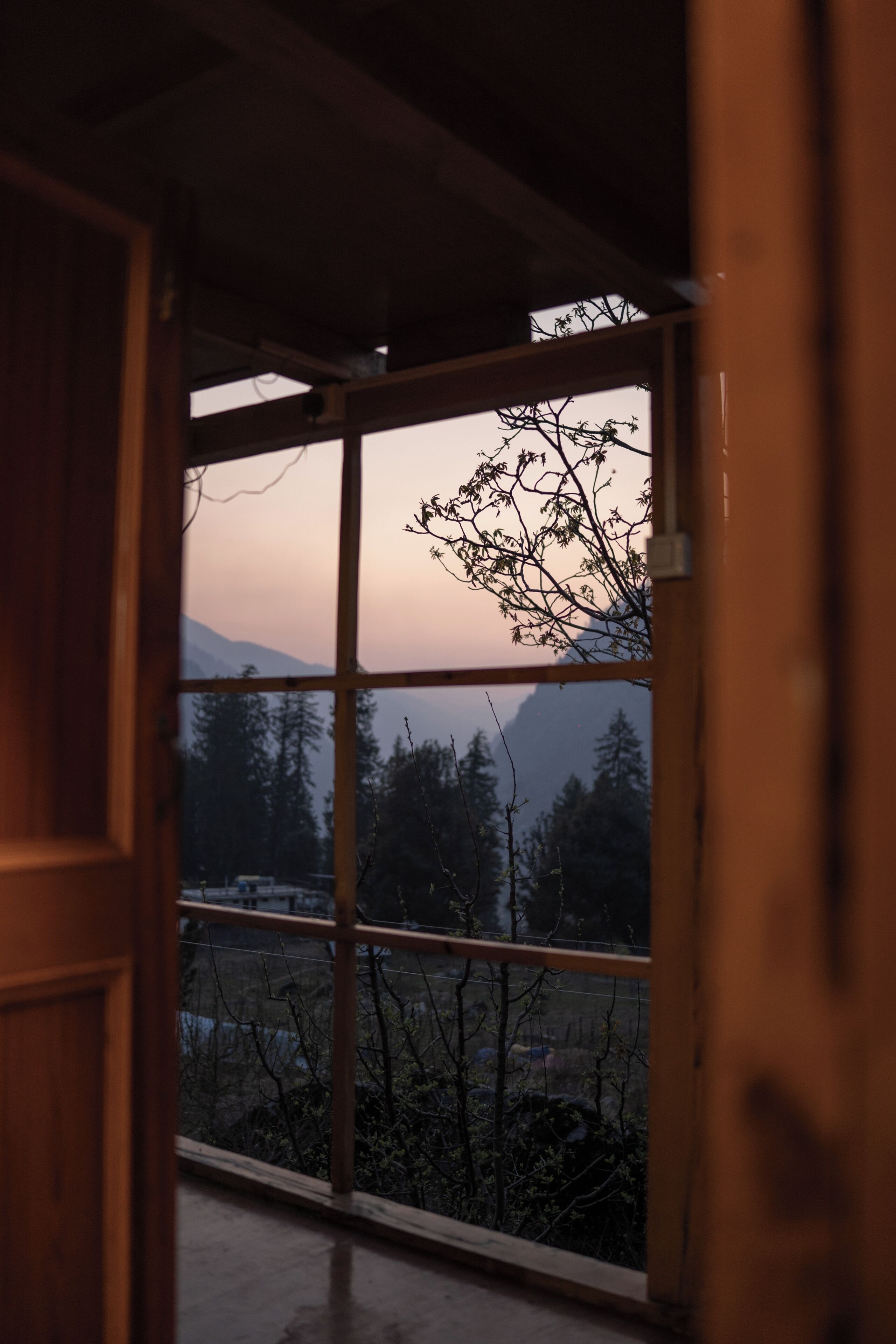 Une pièce dotée d’une grande fenêtre, de poutres en bois et offrant une vue sur les arbres et les montagnes.