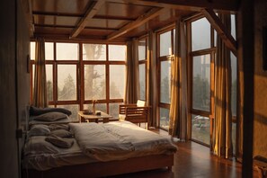 A bedroom with a large bed, a desk, and multiple windows.