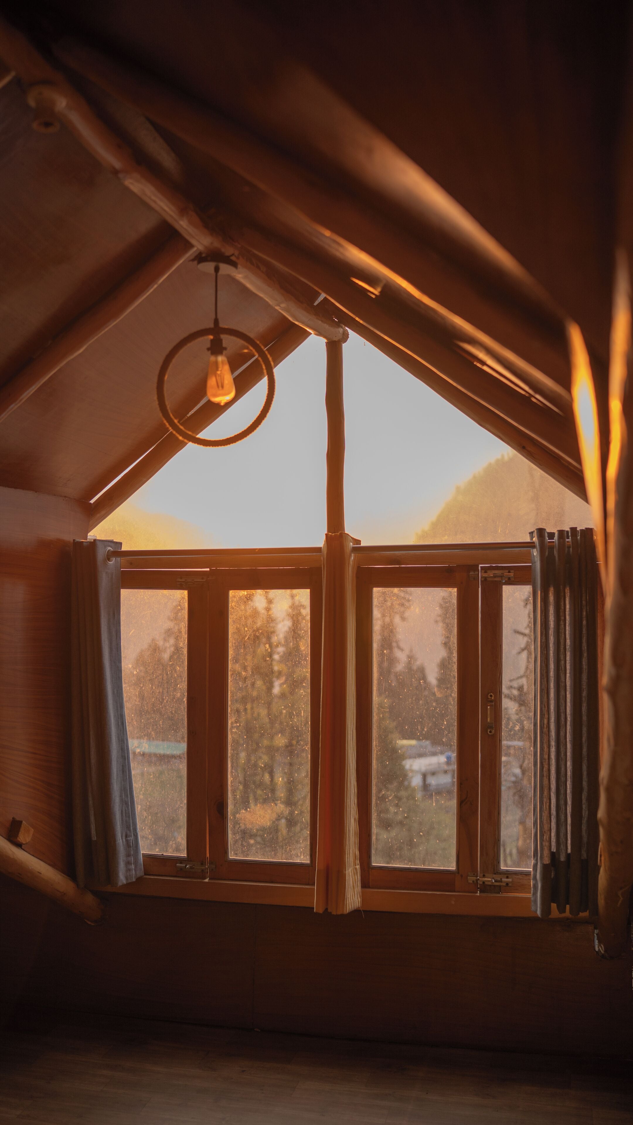 A room with a sloped ceiling, a hanging light fixture, and a large window with curtains.