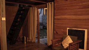 A wooden interior with a chair, a fireplace, a staircase, and a door leading outside. - The Hidden Treasure (Sosan)