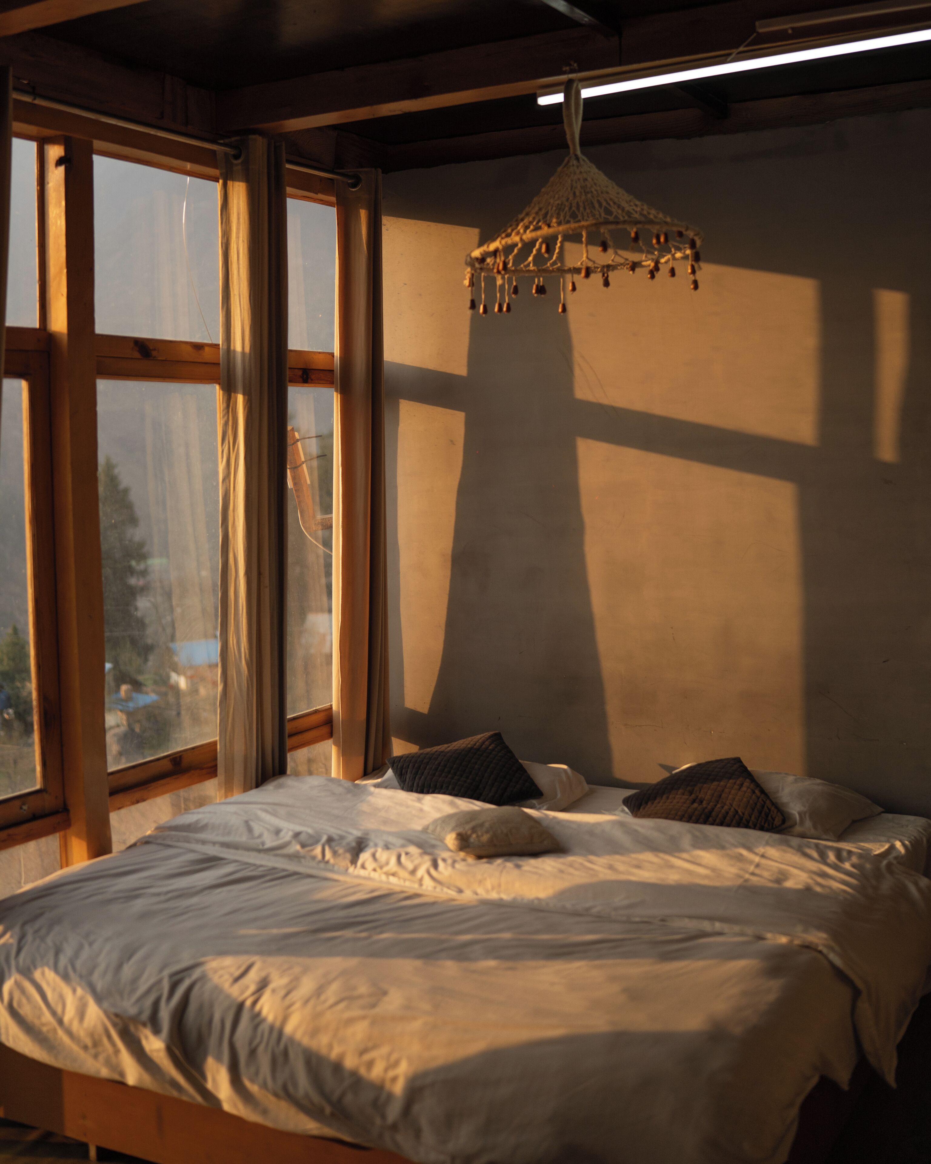Un dormitorio con cama, almohadas, una lámpara colgante y ventanas amplias.