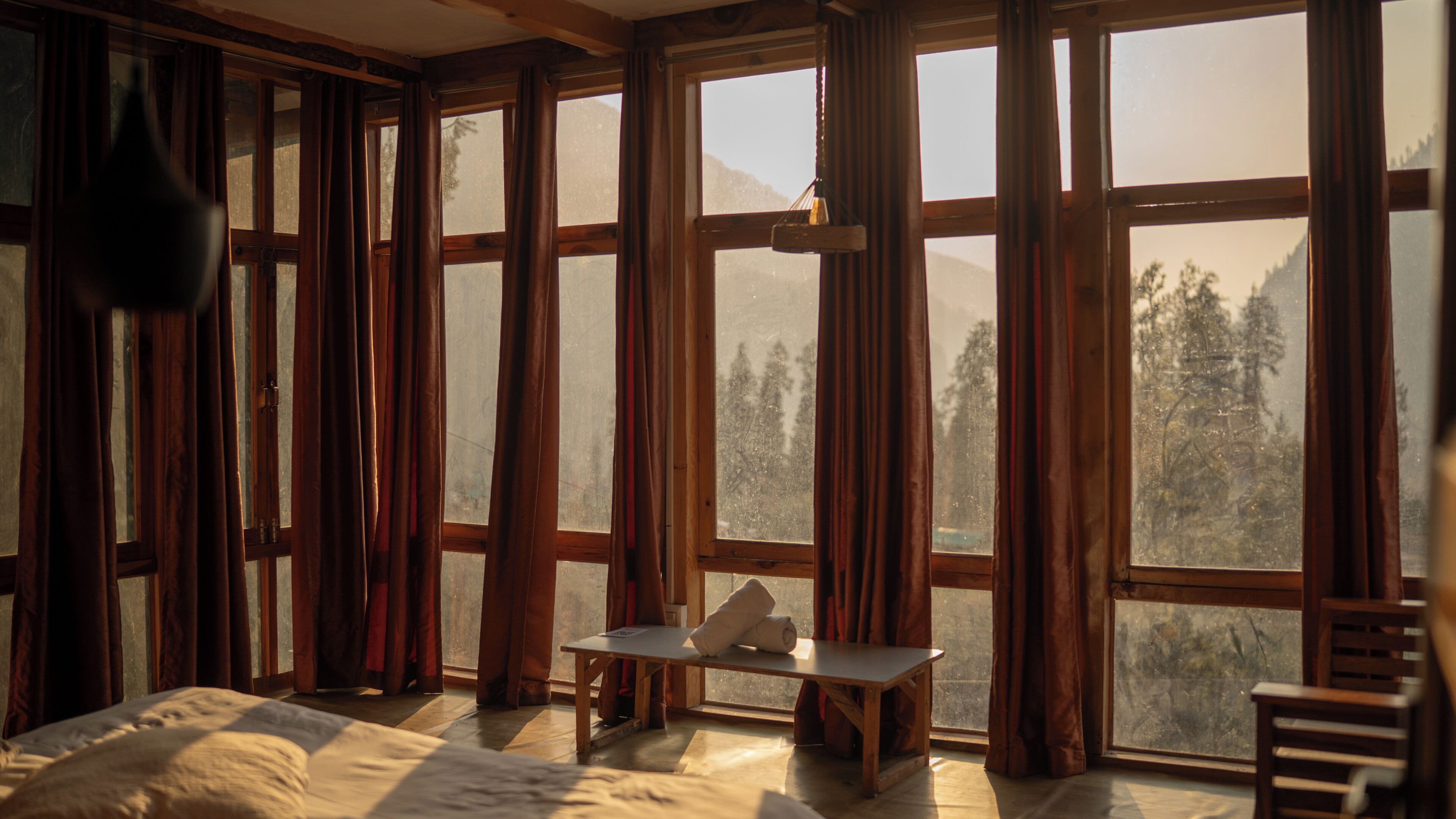 A room with large windows, a bed, a table, and a hanging light fixture.
