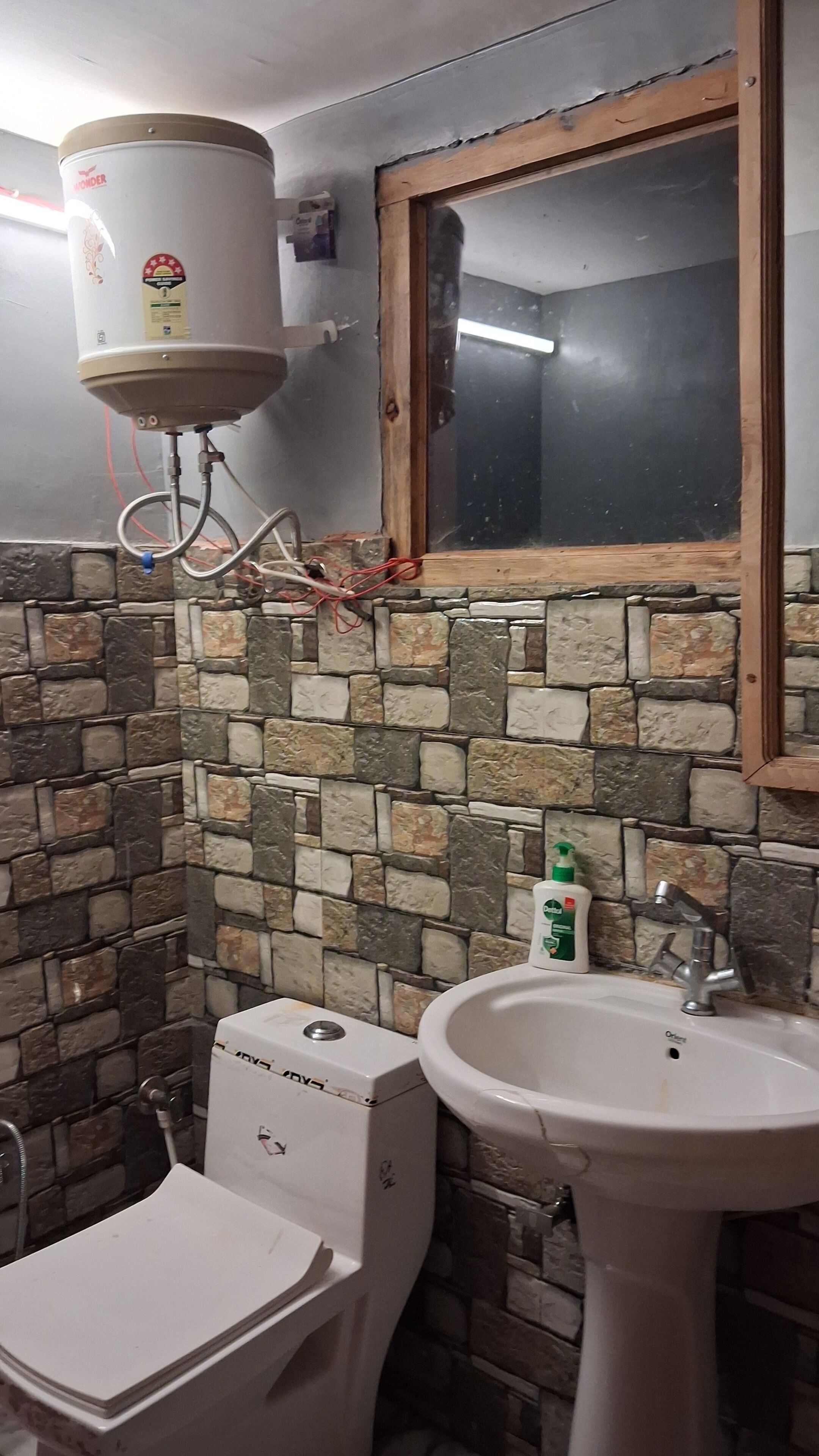 Een badkamer met een stenen muur, een toilet, een wastafel en een boiler.