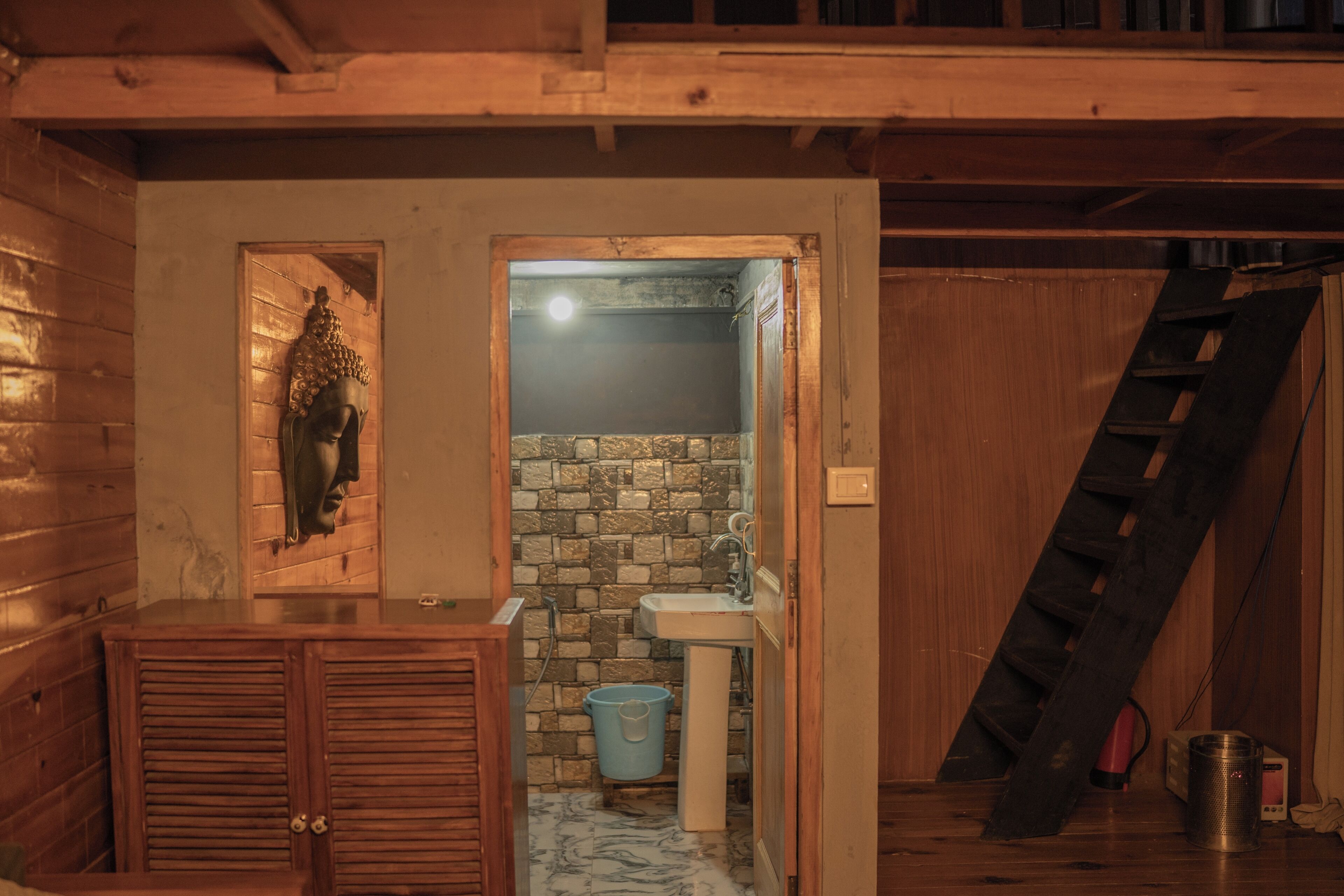 A wooden interior with a bathroom featuring a stone wall, sink, and a blue bucket.