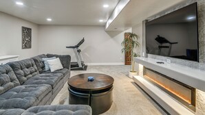 Ein modernes Wohnzimmer mit einem großen Flachbildfernseher, einem grauen Sofa, einem runden Couchtisch und einem Kamin.