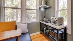 A compact kitchen with a built-in oven, a gas stove, and a stainless steel range hood. There are large windows providing natural light and a view of trees outside. - Commuter's Dream! Cheverly Studio 1/2 Mi to Metro (Cheverly)