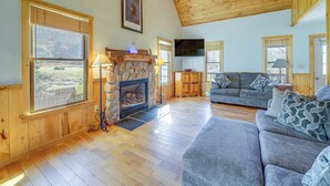 A spacious living room with a stone fireplace, wooden floors, and large windows offering a view of the outdoors. - Scenic Getaway, 10 Mi to Snowshoe Mountain & Lake! (Snowshoe)