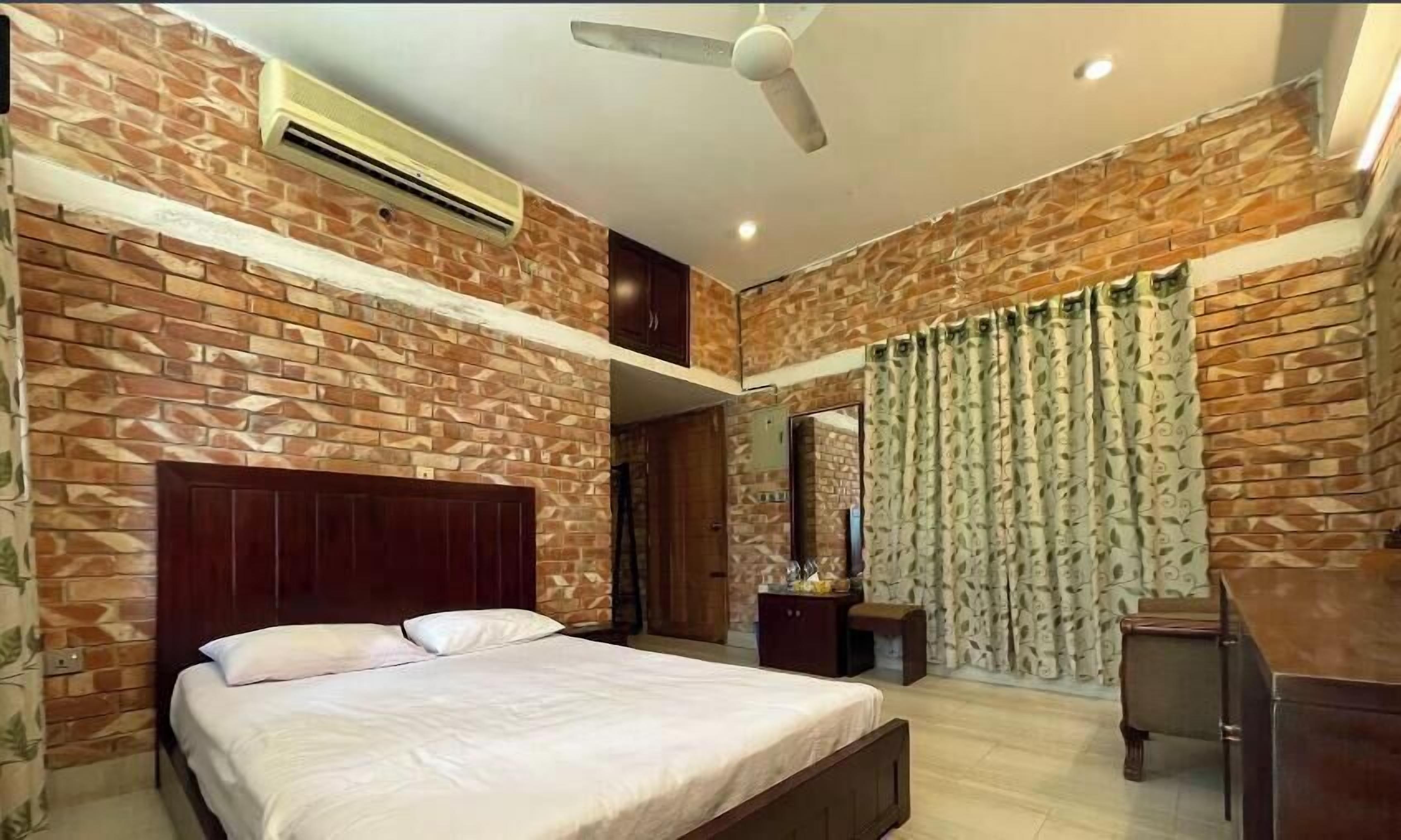 Un dormitorio con pared de ladrillo, una cama, un escritorio y un ventilador de techo.
