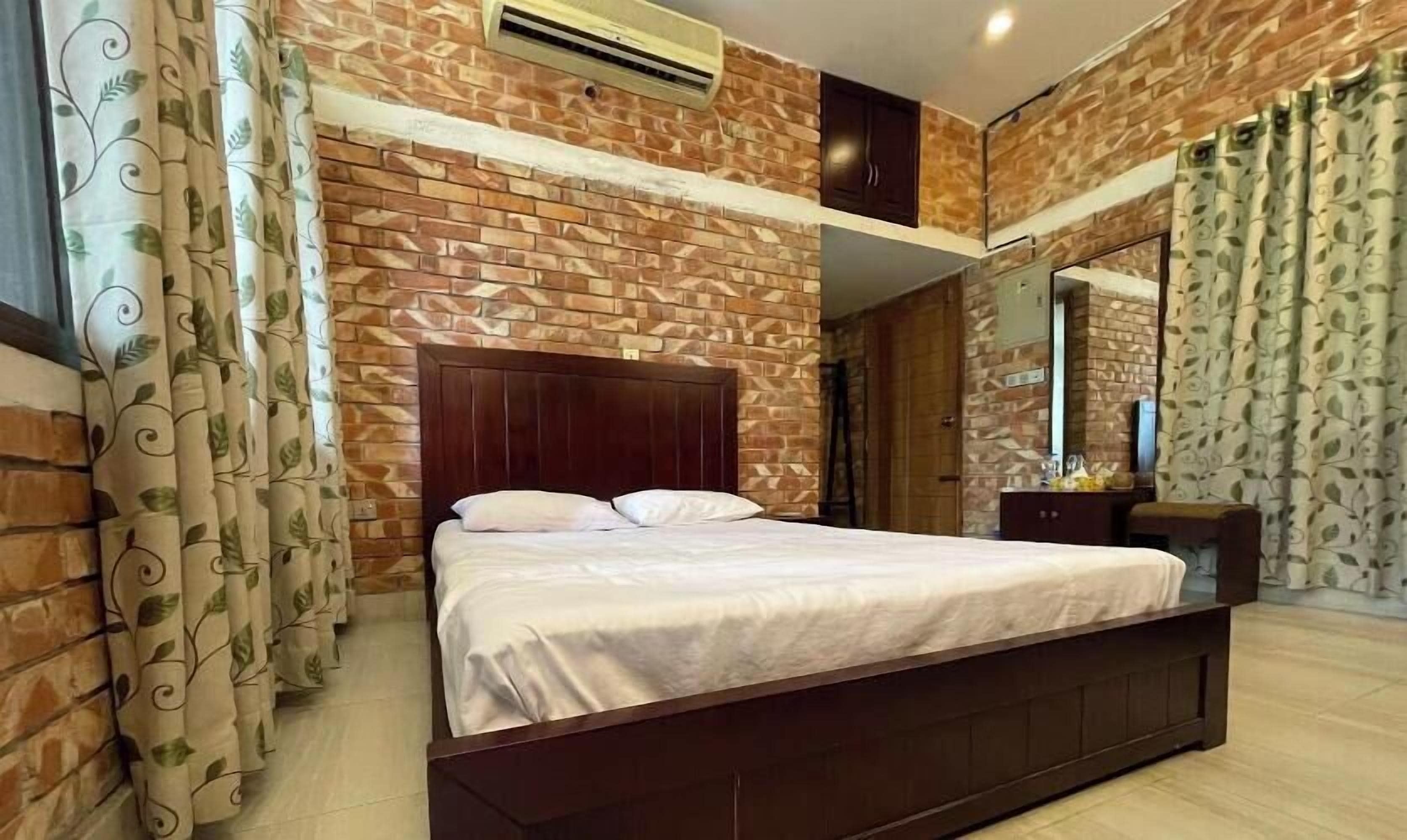 A bedroom with a brick-patterned wall, a wooden bed frame, and curtains with a leaf pattern.