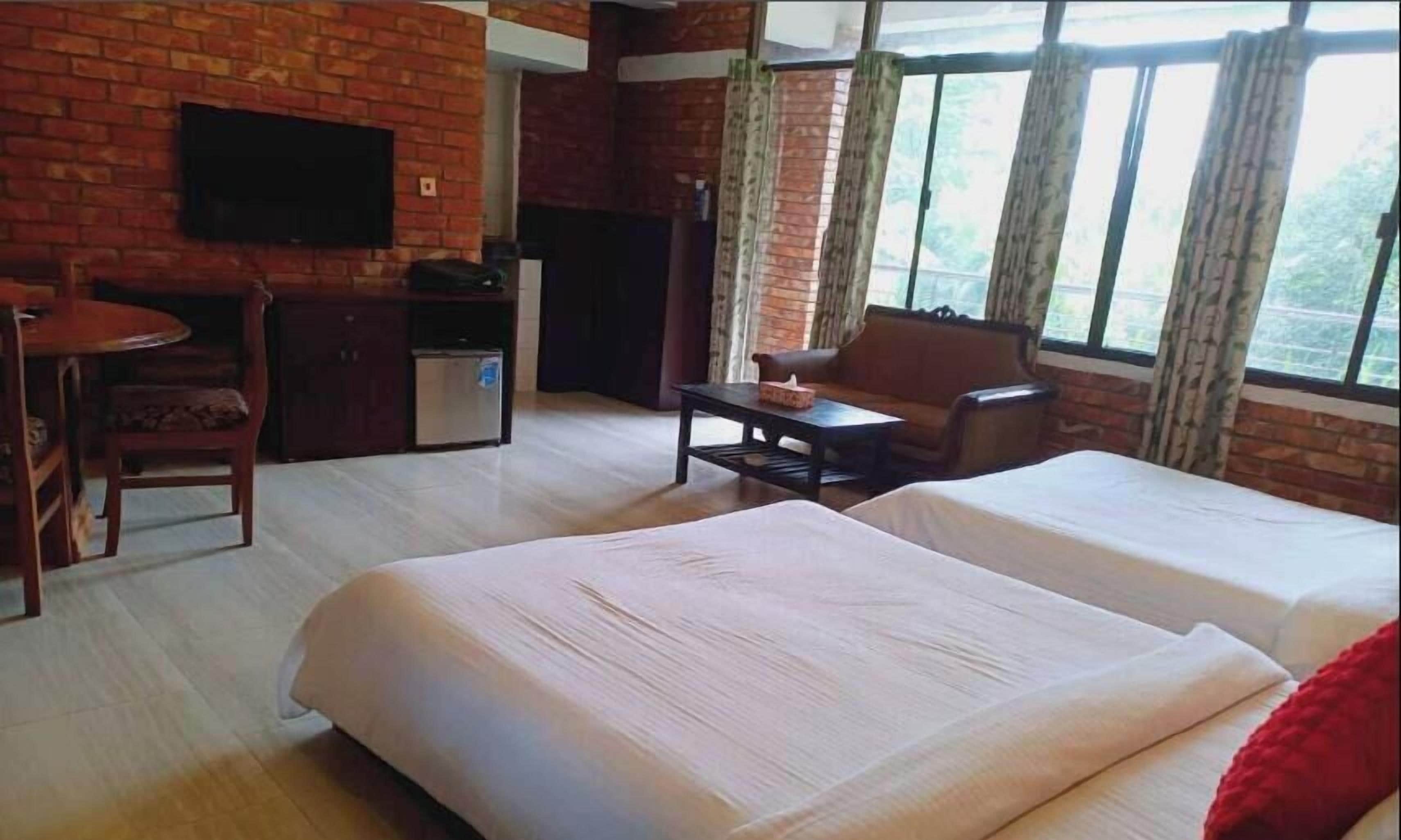 A hotel room with a brick wall, a flat-screen TV, a desk with a chair, a sofa, and two beds.