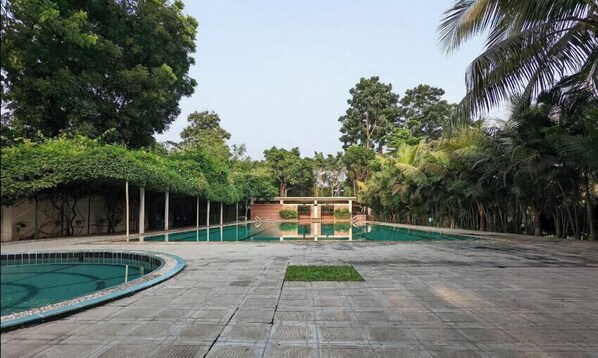 A swimming pool area with a covered seating area and lush greenery. - Chuti Aronnobash Resort (Gazipur)
