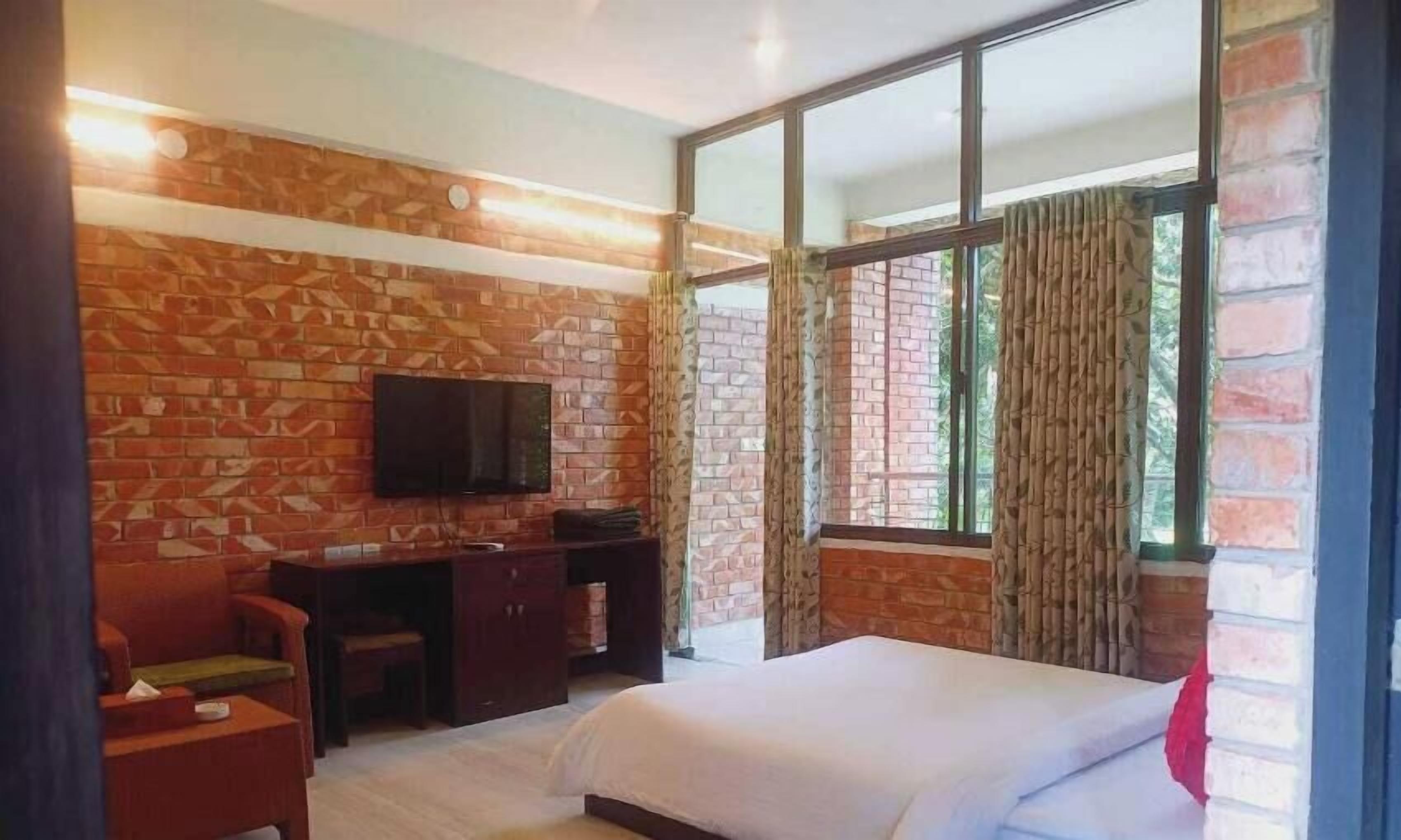 A hotel room with a brick-patterned wall, a bed, a desk with a chair, and a TV.